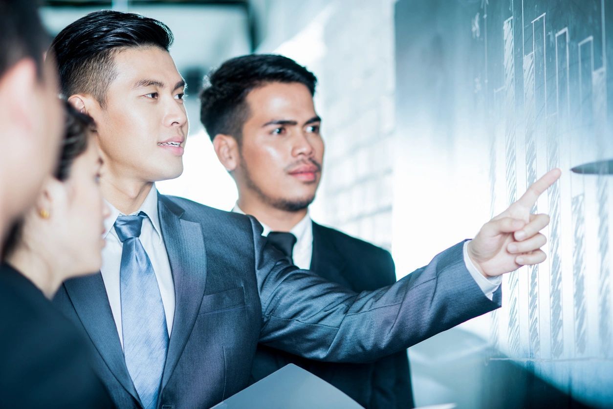 Two men in suits are looking at a whiteboard.